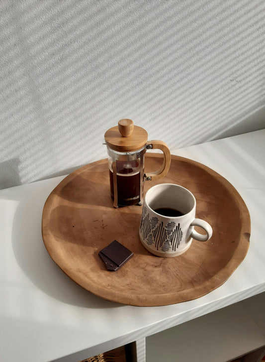 Una taza de café de especialidad humeante junto a varios trozos de chocolate artesanal de distintos porcentajes de cacao, sobre una mesa de madera rústica.