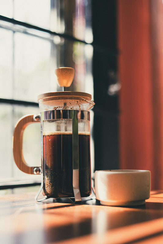 Taza de café filtrado junto a equipo V60, Chemex, Aeropress y Prensa Francesa sobre mesa rústica.