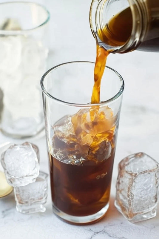 Vaso de cold brew con hielo servido junto a granos de café colombiano en mesa de madera